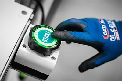 Une main protégée d'un gant de travail actionne un bouton de démarrage