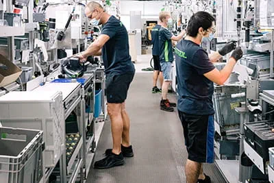Dans l'usine spacieuse, les collaborateurs assemblent les outils électroportatifs sur des postes de travail modernes.