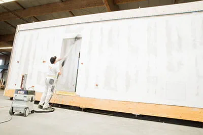 Les murs des maisons préfabriquées sont poncés avec la ponceuse autoportée à rallonges Festool.