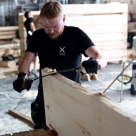 Un constructeur de saunas écorce le bois avec une plane.
