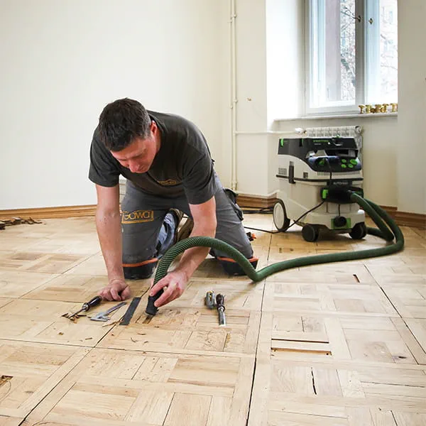 Le maître parqueteur Jarek Gawina dégage les éléments détériorés du parquet et les retire à l'aide de l'aspirateur Festool
